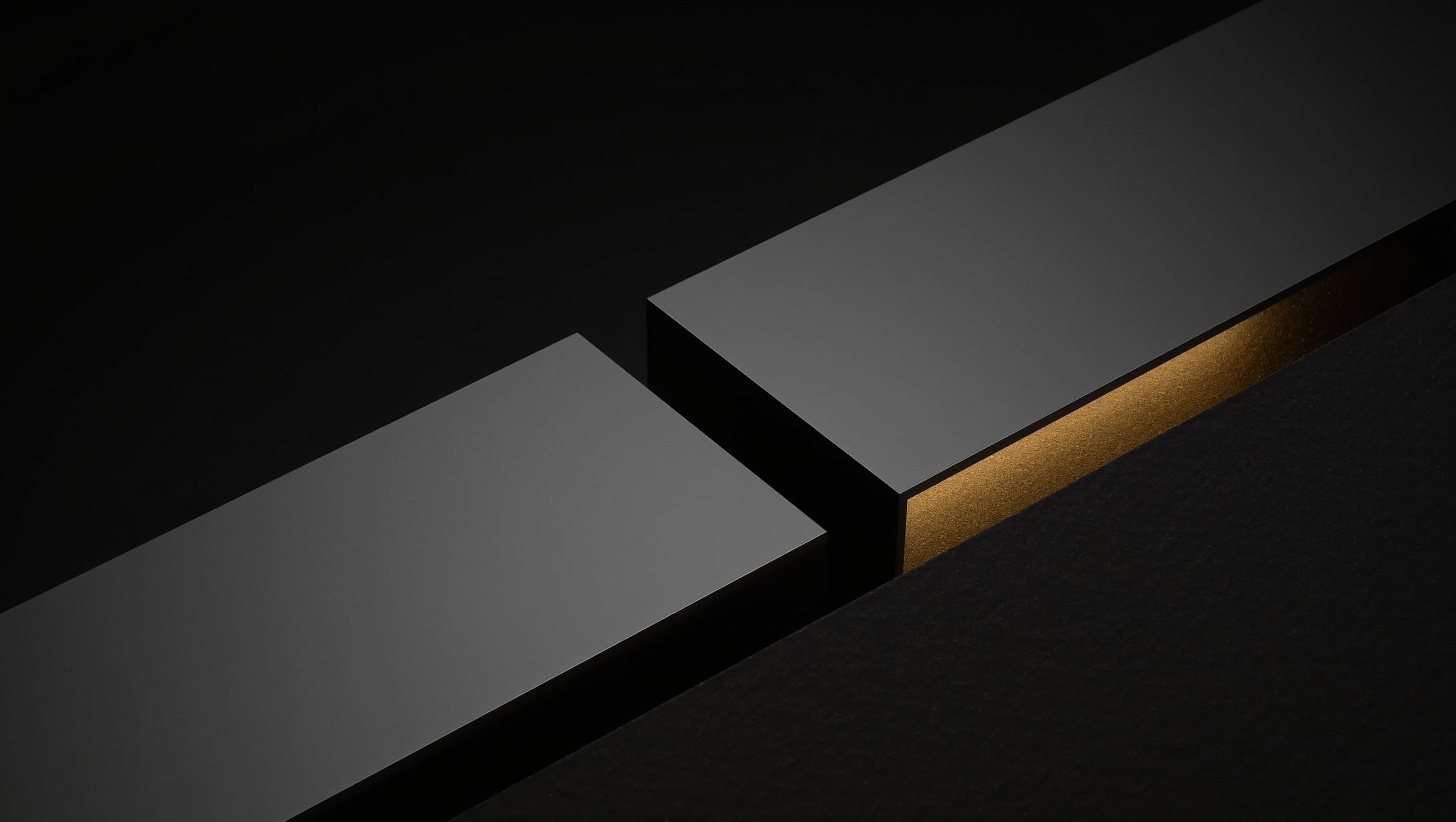 Two machined metal blocks on a dark surface, separated by a narrow gap, with warm light along the inner edge of one of them.